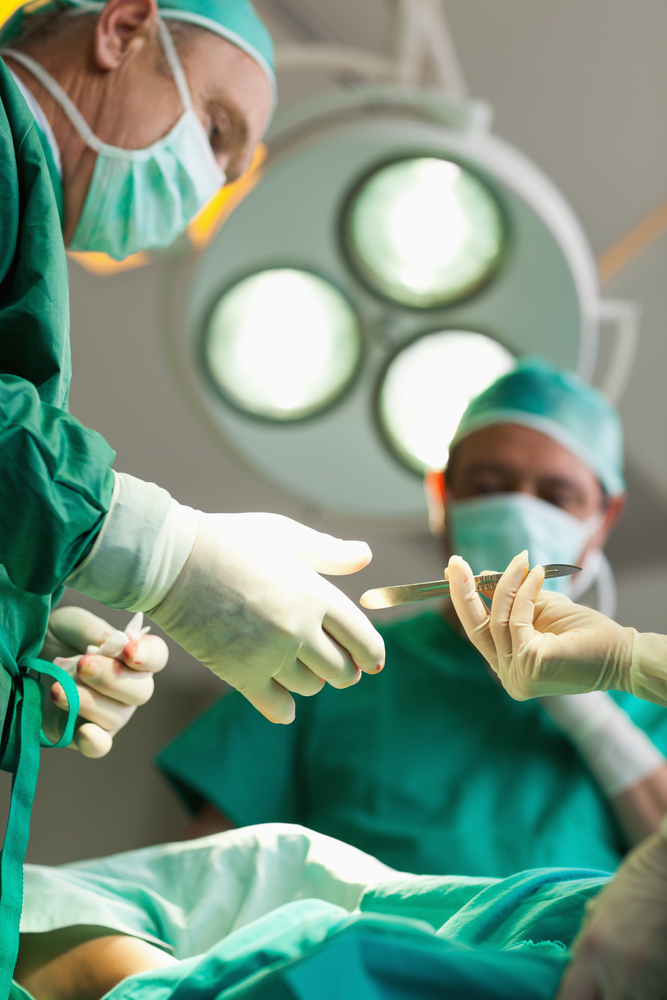 Surgeon taking a scalpel from a gloved hand in a surgical room